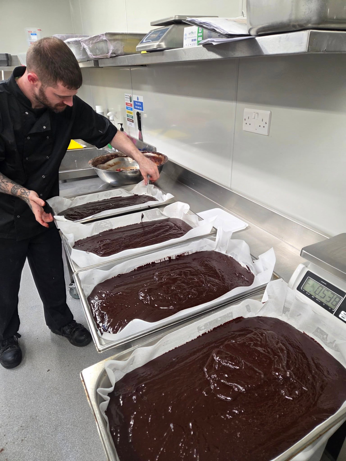 Chef spreading chocolate brownie mix across trays